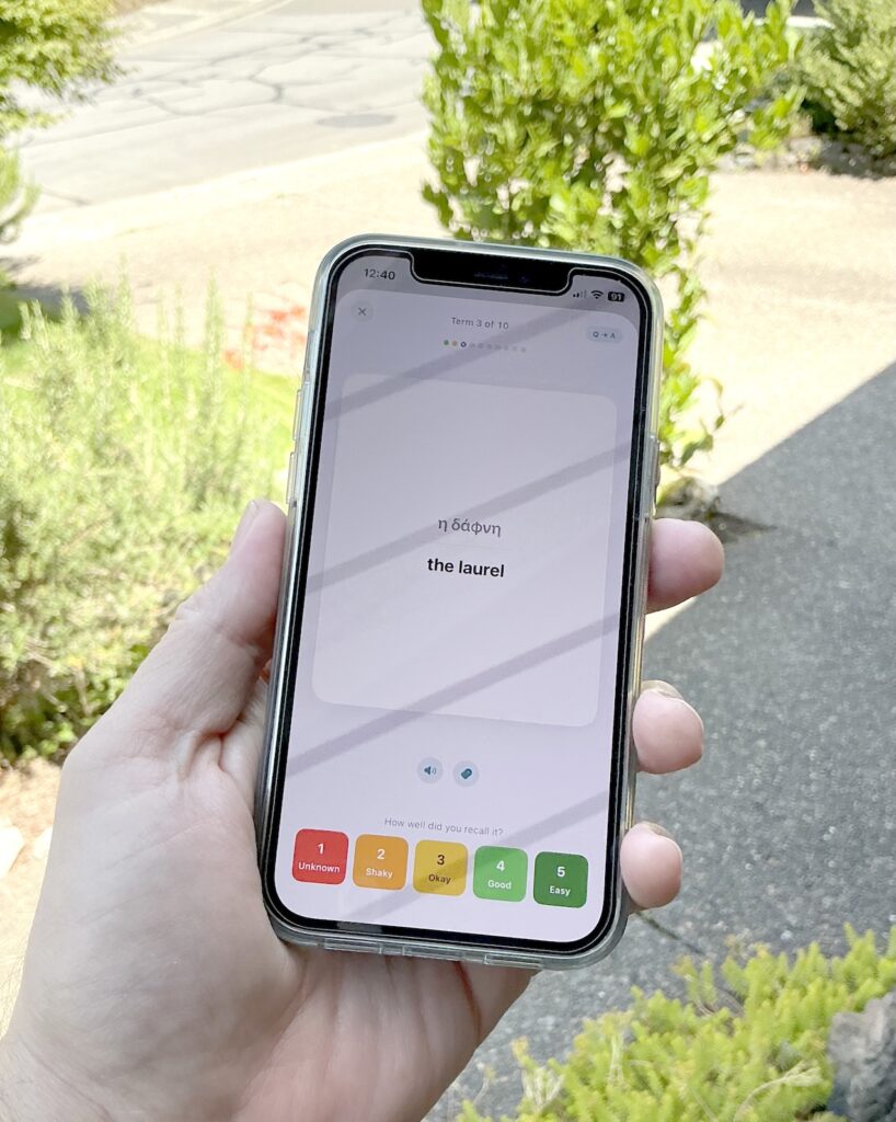 An iPhone held outdoors, showing a flashcard drill in the Lexolotl app